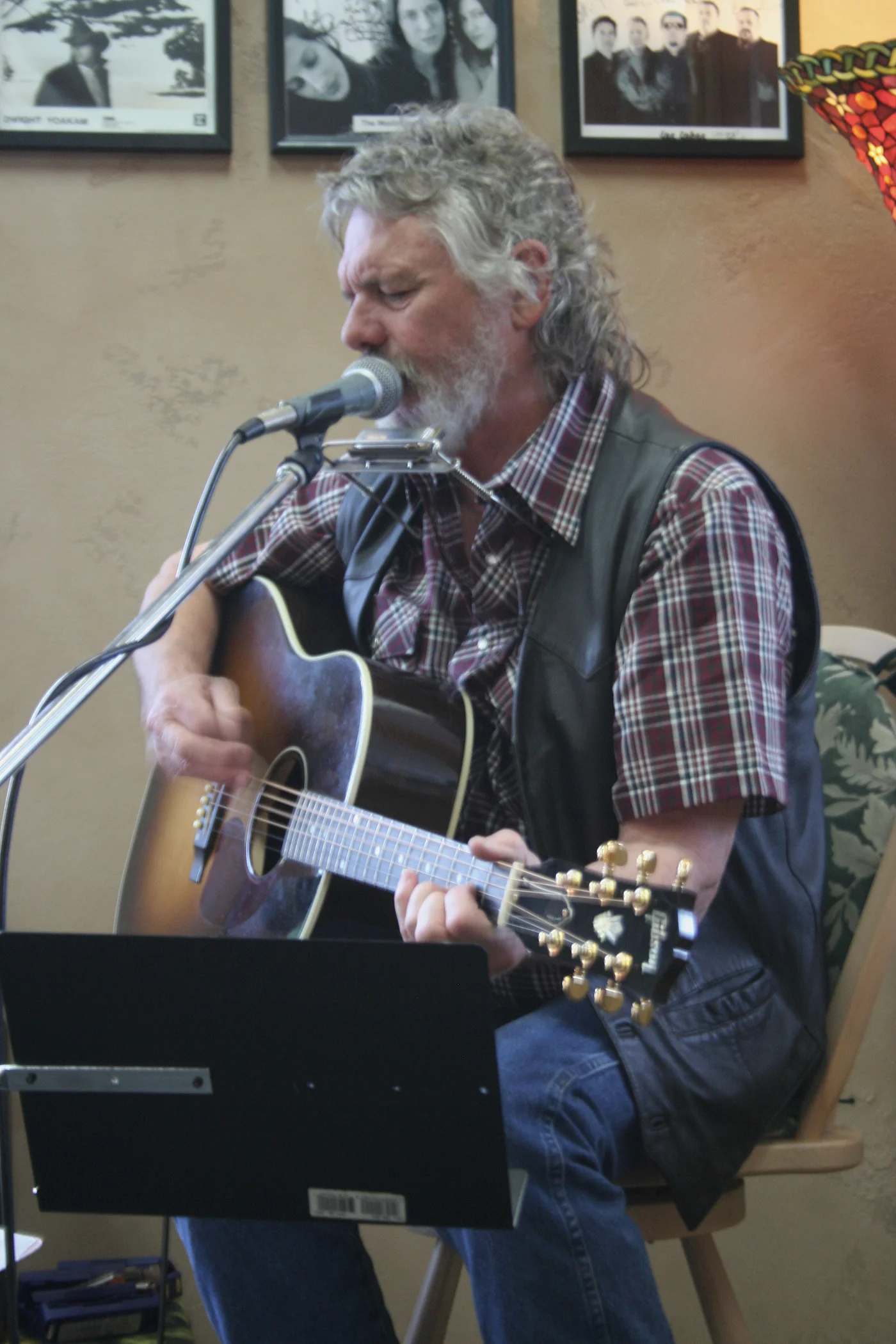 Michael Seward seated with his acoustic guitar, microphone and harmonica during a MusicFest performance